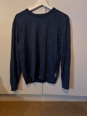 Mörkblå tröja från Lindbergh White - Snygg mörkblå tröja från Lindbergh White med rund halsringning och diskret logga på bröstet. Tröjan har långa ärmar och är tillverkad i ett tunt, mjukt material som passar perfekt till lager på lager. Enkel och stilren design.