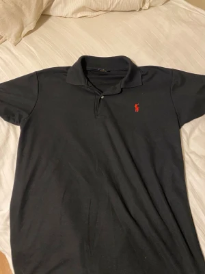 Polo Piké black shirt - Säljer nu en polo piké i svart med röd logga, storlek M men passar också L och S, använd 5 gånger