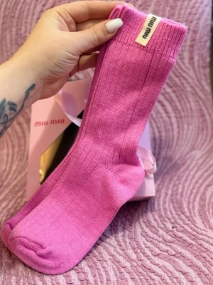Ribbstickade rosa strumpor från Miu Miu - Snygga ribbstickade strumpor från Miu Miu i en härlig rosa färg. Strumporna har en klassisk form och är prydda med en diskret Miu Miu-logga upptill. Perfekta för att addera lite färg till din outfit.