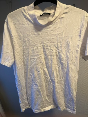 Vit t-shirt med hög krage från Jack n Jones  - En basic vit t-shirt från Jack n Jones med hög krage och klassisk passform. Tillverkad i mjuk bomull och har korta ärmar. Perfekt att styla lager på lager eller bära som den är.