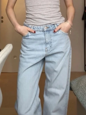 Ljusa baggy jeans från Monki - Säljer ett par ljusblå baggy/straightleg jeans från Weekday med mellan midja och raka, vida ben. Klassisk femficksmodell med knappgylf och läderpatch bak i midjan. Perfekta för en avslappnad och trendig look. 