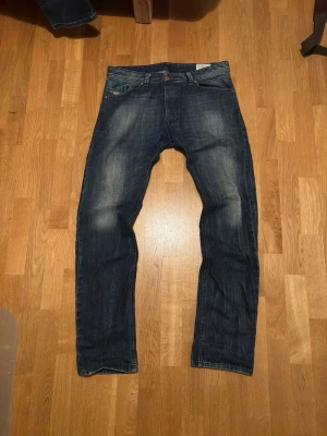 Vintage Diesel Jeans - Snygga mörkblå diesel jeans med raka ben och klassisk femficksdesign. Jeansen har en lätt tvättad look med slitningar på framsidan och är tillverkade i jeansmaterial. Perfekta för en avslappnad stil. Storlek 34/34