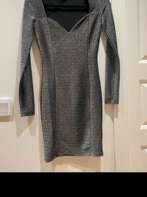 Glittrig silverklänning Gina Tricot - Supersnygg glittrig silverklänning från Gina Tricot med lång ärm och figurnära passform. Klänningen har en v-ringad urringning och är perfekt för dig som vill sticka ut. Materialet är stretchigt och skimrar snyggt i ljuset.