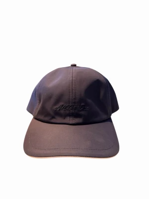 Blå keps från All Cap One - Stilren svart keps från All Cap One med broderad logga framtill. Klassisk sexpaneldesign och böjd skärm. Kepsen har elastiskt band baktill för skön passform. Materialet är slätt och lätt, perfekt för en avslappnad look.