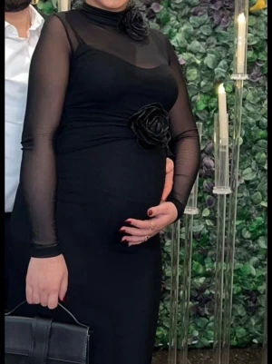 Svart långklänning med meshärmar - Elegant svart långklänning med transparenta meshärmar och höghalsad design. Klänningen har dekorativa svarta blommor vid halsen och midjan för en extra detalj. Perfekt för dig som vill sticka ut med stilren look. Funkar utmärkt för gravida och som vill känna sig extra eleganta och söta. Pris går att diskutera.
