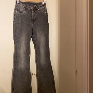 Grå bootcut jeans från Divided, stl 32 - Grå jeans från Divided i bootcut-modell med hög midja. Jeansen har en tvättad look och råa, fransiga benslut för en cool vibe. Klassisk femficksdesign och tillverkade i denim. Perfekta för dig som gillar en avslappnad men trendig stil. Highwaist modell.