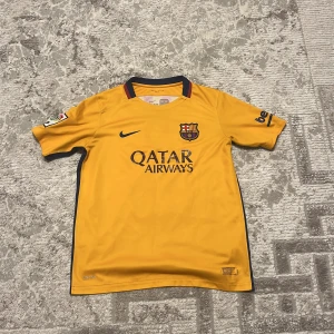 Gul FC Barcelona matchtröja Nike - FC Barcelona matchtröja i gul färg med mörkblå detaljer och klubbmärke på bröstet. Nike Dri-Fit material för skön känsla och ventilation. Kortärmad med LFP-patch på ena ärmen och Beko-logga på andra. För 13-15 år