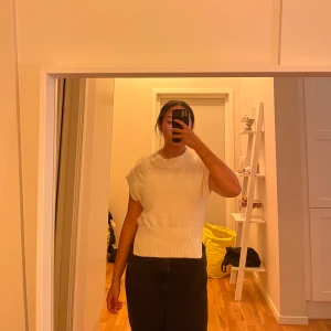 Vit stickad ärmlös tröja - Säljer en vit stickad tröja utan ärmar med hög hals och ribbad nederkant. Tröjan har en avslappnad passform och slits i sidorna, perfekt att styla över en skjorta eller t-shirt. Enkel och clean look som funkar året runt.