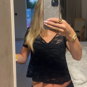 Svart spetsblus med v-ringning - Säljer en svart blus i spets med v-ringning och korta ärmar. Toppen har en lätt croppad passform och fina rynkdetaljer framtill. Perfekt för dig som gillar en feminin och trendig look.