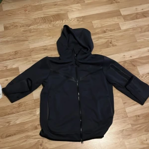 Navy blå Nike hoodie med dragkedja M - Svart hoodie från Nike i storlek M med hel dragkedja framtill och huva. Tröjan har långa ärmar med tumhål och en extra ficka med dragkedja på ena ärmen. Perfekt för träning eller chill. Snygg och sportig design.