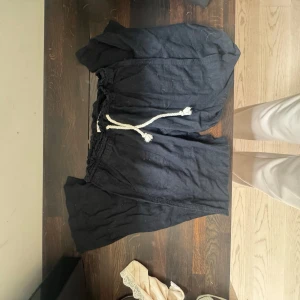 Svarta linnebyxor med snörning - Svarta, linnebyxor med vit snörning i midjan. Tillverkade i ett mjukt linnematerial som känns chill och luftigt. Perfekta för varma dagar när du vill ha något bekvämt och snyggt.