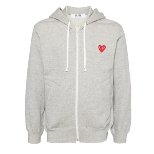 CDG hoodie - Grå hoodie med dragkedja och huva från Comme des Garçons. Tröjan har ett rött hjärta med ögon broderat på bröstet, vita snören och två fickor framtill. Det är herrstorlek🙌 Hör av dig vid minsta fundering så hjälper vi dig!😃