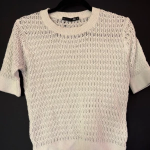 Vit stickad kortärmad tröja 157 - Säljer en vit stickad tröja från 157 med korta ärmar och rund hals. Tröjan har ett snyggt hålmönster över hela och ribbade muddar vid ärmslut och nederkant. Perfekt för lager-på-lager och en fräsch look till våren!