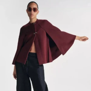 Vinröd cape  - Säljer en vinröd cape-kappa med vida, svepande ärmar och snygg knäppning framtill. Jackan har en elegant och stilren look, perfekt för dig som vill sticka ut. Materialet känns mjukt och har en lyxig känsla. Helt slutsåld