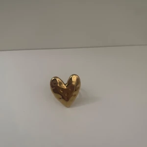 Guldig hjärtformad ring - Cool ring i guldigt metall med hjärtformad design. Ringen har en blank, lite vågig yta som ger en unik look. Perfekt accessoar för att lyfta din outfit med en söt och trendig detalj.