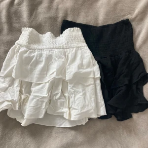 Två pack Volangkjolar  - Två korta kjolar från SHEIN i storlek XS, en vit och en svart. Båda har bred smock i midjan och flera lager volanger som ger en snygg och flowy look. Perfekta för att skapa en trendig outfit med lite extra attityd.