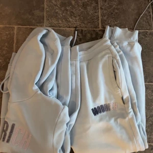 Ljusblå mjukisdress från hoodrich - Säljer ett par ljusblå mjukisbyxor från Hoodrich med broderad logga i blått och rosa på ena benet. Byxorna har dragsko i midjan och sidofickor. Perfekta för chill dagar eller när du vill vara extra bekväm.