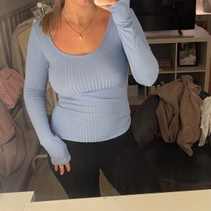 Ljusblå ribbad långärmad topp - Säljer en ljusblå långärmad topp med ribbad struktur och djup ringning både fram och bak. Toppen är figurnära och har en mjuk, stretchig känsla som gör den superbekväm. Perfekt att styla med jeans eller kjol för en fräsch look.
