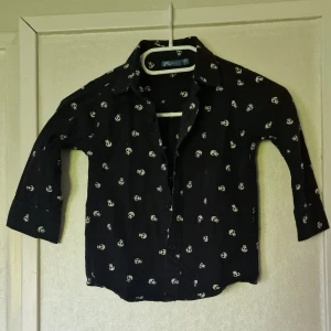 Svart skjorta med dödskallemönster - Svart skjorta från X-Max med vita dödskallar över hela tyget. Skjortan har klassisk krage, långa ärmar och knäppning framtill. Skjortan kan vara något tvättpåverkad i färgen.