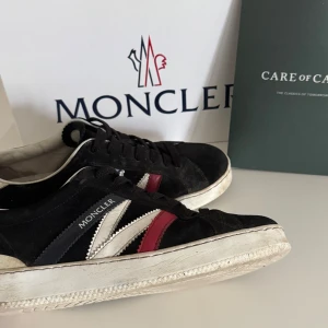 Moncler sneakers i mocka och skinn - Snygga Moncler sneakers i svart mocka med vita och röda detaljer i skinn. Klassisk låg modell med vit sula och snörning. Moncler-logga på sidan och hälen. Perfekta för dig som gillar streetstyle och vill sticka ut med exklusiva detaljer. Skorna kommer bli rengjorda innan dom skickas ut.. obs pris kan diskuteras vid snabb köp 