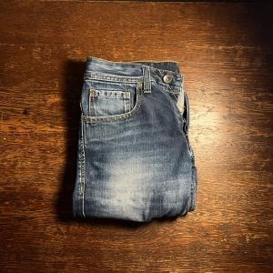 Blå jeans från Jack & Jones - W29 L34. Snygga blå jeans från Jack & Jones med klassisk femficksdesign och slitna detaljer. Jeansen har kontrastsömmar och en liten logotypdetalj vid fickan. Perfekta för dig som gillar en avslappnad och stilren look.