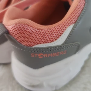 Stormberg sneakers i grått och korall - Snygga sneakers från Stormberg i grått med korallfärgade detaljer och snörning. Ovandelen är i mesh och syntet för bra andningsförmåga. Skorna har vit och svart sula med coolt mönster och rund tå. Perfekta för dig som gillar sportig stil.