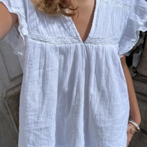 Vit blus - Säljer en luftig vit blus med v-ringning, volangärmar och fina spetsdetaljer över bröstet. Blusen är tillverkad i ett mjukt, lätt bomullstyg och har en avslappnad, loose passform. 