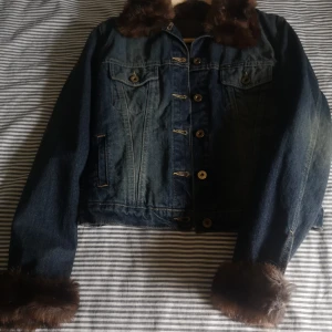 Fodrade Jeansjacka Med Fuskpälsdetaljer - Stl S. Säljer en helt ny jeansjacka från Frankrike med bruna fuskpälsdetaljer på krage och ärmslut. Jackan har knappar framtill, två bröstfickor med lock och quiltat foder på insidan. Perfekt för dig som vill ha en unik och varm denimlook, rök och djurfri hem. Kan hämtas i Norra Stockholm. 