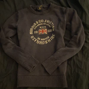 Mörkblå stickad tröja Morris Gents S - Snygg mörkblå stickad tröja från Morris Gents med tryck och Union Jack-flagga på bröstet. Tröjan har ribbade muddar vid ärmslut och nederkant samt rund halsringning. Perfekt för dig som gillar brittisk stil och vill ha något som sticker ut.