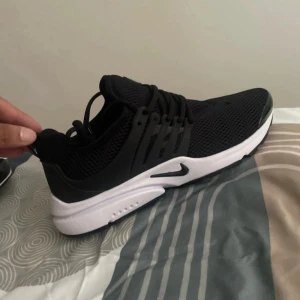 Nike Presto svarta sneakers - Svarta Nike Presto sneakers med vit sula och mesh-överdel. Skorna har snörning och en sportig, modern look med rund tå och platt sula. Perfekta för dig som gillar stilrena och bekväma sneakers med en clean vibe.