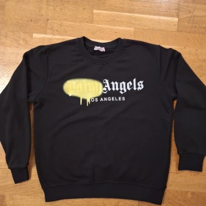 Svart Palm Angels sweatshirt M - Svart sweatshirt från Palm Angels i 100% bomull med klassisk rund hals och tryck framtill i vitt och gult. Tröjan har långa ärmar och ribbade muddar vid ärmslut och nederkant. Snygg streetwear-vibe med Los Angeles-tryck.
