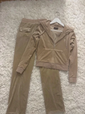 Juicy couture tracksuit - Jättefint juicy sett i beige. Mycket bra skick på båda utom att byxorna tappat en metall sak på snöret. Säljer båda för 820kr eller 480kr/st. Nypris 2400kr för båda. 