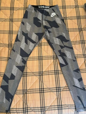 Nike leggings med grått camomönster - Nike leggings i storlek S med grått och svart camouflagemönster. Elastisk midja med 'JUST DO IT' tryck på insidan och Nike-logga på höften. Tight passform och stretchigt material som är perfekt för träning.