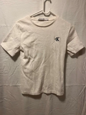 Vit t-shirt från Calvin Klein  - Snygg vit t-shirt från Calvin Klein Jeans med klassisk rund hals och korta ärmar. Diskret CK-logga broderad på bröstet ger en clean och stilren vibe. Tillverkad i mjuk bomull som känns skön mot huden. Perfekt för dig som gillar minimalistisk stil.