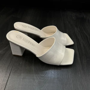 Vita klackskor - Stilrena vita klackskor från Boohoo med fyrkantig tå. Skorna har en blockklack och ett diskret mönster. 