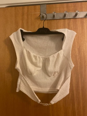 Vit croppad linnetopp med kedjedetalj - Säljer en vit croppad linnetopp med grovstickad struktur och breda axelband. Toppen har en snygg guldfärgad kedjedetalj och dragkedja i sidan för enkel påklädning. Står strl L men tycker de passar även M och kanske mindre strl. 