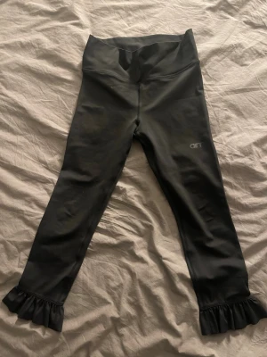 Svarta leggings från Aim'n med volang - Snygga svarta leggings från Aim'n med hög midja och volangdetaljer vid bensluten. Perfekta för dig som vill ha något extra till träningspasset eller bara gillar coola detaljer. Stretchigt material som sitter skönt och följer kroppen.