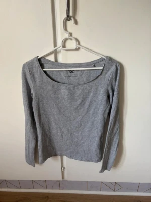 Grå långärmad topp från Lager 157 - En enkel och stilren grå långärmad topp från Lager 157 i storlek XS. Toppen har rundad halsringning och är gjord i mjuk bomullsblandning med lite stretch för skön passform. Perfekt att matcha med jeans eller kjol.