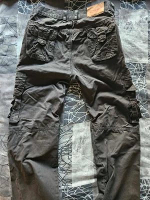 Motorcykelbyxor från Course, 36/32 - Säljer ett par svarta motorcykelbyxor med flera praktiska fickor på både fram- och baksida samt på benen. Byxorna har knapp och dragkedja i midjan och är tillverkade i bomull. Fickor för knäskydd.