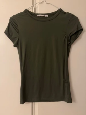Olivgrön kortärmad t-shirt - En enkel och stilren olivgrön t-shirt med rund hals och korta ärmar. Modellen är figurnära och passar perfekt till jeans eller shorts. Materialet känns mjukt och lätt mot huden, vilket gör den skön att bära hela dagen.