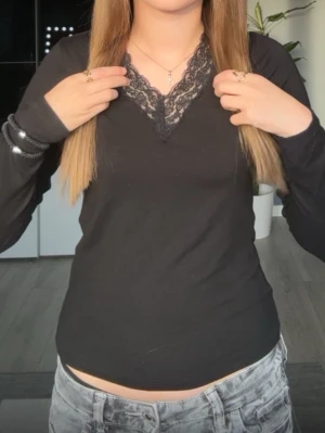 Svart långärmad topp med spets - Säljer en svart långärmad topp med v-ringning och snygg spetsdetalj vid halsen. Toppen har en figurnära passform och är perfekt att styla med jeans eller kjol. Materialet känns mjukt och stretchigt, vilket gör den bekväm att bära hela dagen.