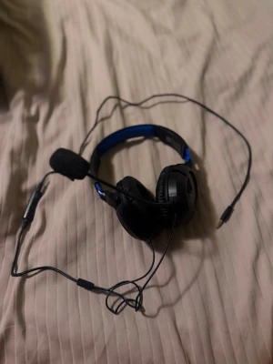 Mikrofon - Kabelanslutet spelheadset med mikrofon, svart och blå design. Utrustad med 3,5 mm kontakt och justerbar mikrofon. Passar för gaming och kommunikation. Synligt i gott skick utan tydliga tecken på slitage eller defekter
