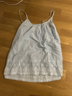 Ljusblå linnetopp från Hampton Republic - Säljer min ljusblåa linnetopp från Hampton Republic i storlek S. Toppen har tunna axelband, smockad rygg och vita broderade blommor längs nederkanten. Materialet är bomull och toppen har en lätt randig struktur. Perfekt för varma sommardagar!💕