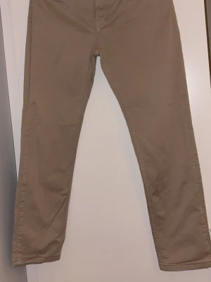 Beige chinos från Denimes - Snygga beige chinos från Denimes med klassisk femficksdesign och knappstängning fram. Byxorna har raka ben och normal passform, tillverkade i mjuk bomull som är skön att bära. Perfekta för dig som gillar stilrena och enkla byxor.