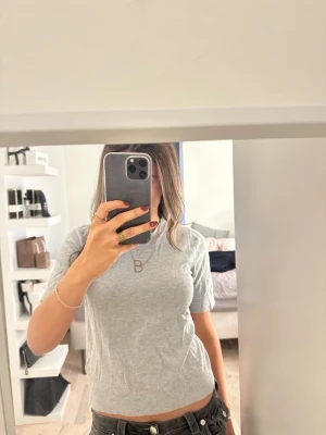 Ljusgrå kortärmad stickad tröja - Säljer en ljusgrå, kortärmad stickad tröja med rund hals. Tröjan har en enkel och clean look, perfekt till jeans eller kjol. Materialet känns mjukt och följsamt, och modellen sitter snyggt utan att vara för tight.