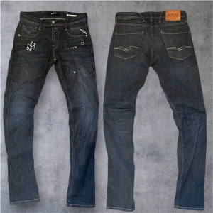 Selvedge replay anbass  - Mörkblå Replay Anbass jeans med snygga slitningar och patchdetaljer framtill. Klassisk femficksmodell med kontrastsömmar och logotyp på bakfickan. Jeansen har en rak passform och är gjorda i slitstarkt denimtyg. Perfekt för dig som gillar en cool och avslappnad stil.