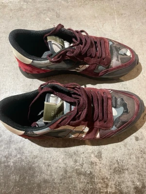 Valentino Garavani Rockrunner sneakers - Säljer ett par Valentino Garavani Rockrunner sneakers med vinröda mockadetaljer och coolt camouflage-mönster i grått, svart och beige. Skorna har snörning, platt sula och rund tå. Perfekt för dig som gillar statement pieces och exklusiva märken. Pris kan diskuteras 