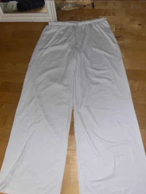 Vita mjukisbyxor från H&M Divided - Säljer ett par vita mjukisbyxor från H&M Divided i storlek S. Byxorna har elastisk midja och är tillverkade i mjukt bomullsmaterial. Passformen är loose och modellen är rak med breda ben, perfekt för chill dagar. Aldrig använda 