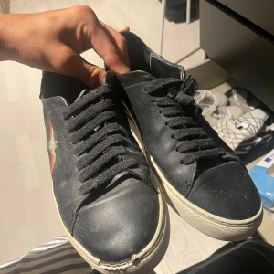 Arigato svarta sneakers med broderade fåglar - Svarta sneakers från ARIGATO med broderade färgglada fåglar på sidorna. Skorna har vita sulor, svarta snören och är tillverkade i skinn. Perfekt för dig som vill ha en unik detalj på dina skor. Säljer för de är alldeles för stora på mig. Bra pris så passa på😁😁