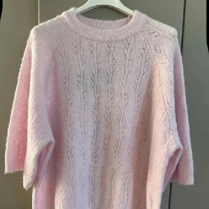 Ljusrosa stickad tröja från danska Kaffe - Superfin ljusrosa stickad tröja från danska Kaffe Tröjan har ett snyggt hålmönster, rund hals och ribbade muddar. Perfekt för dig som gillar mjuka och lyxiga material. Passar dig som vill ha en chill och feminin look.